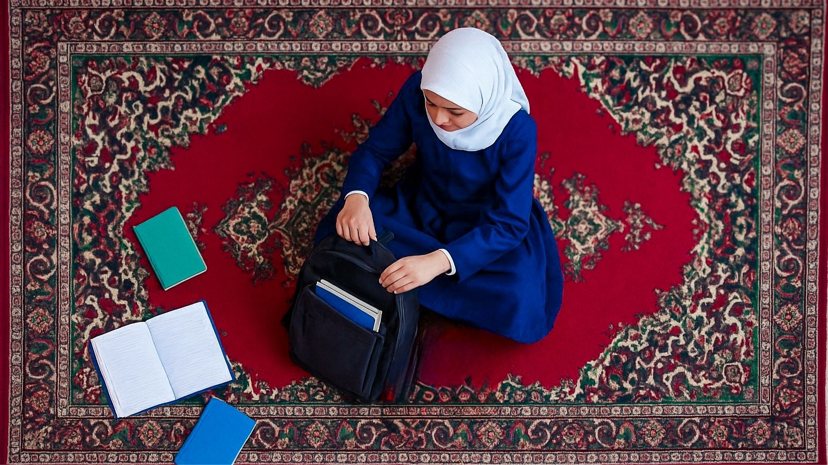 Mädchen mit Kopftuch packt Bücher in ihren Schulrucksack, von oben fotografiert