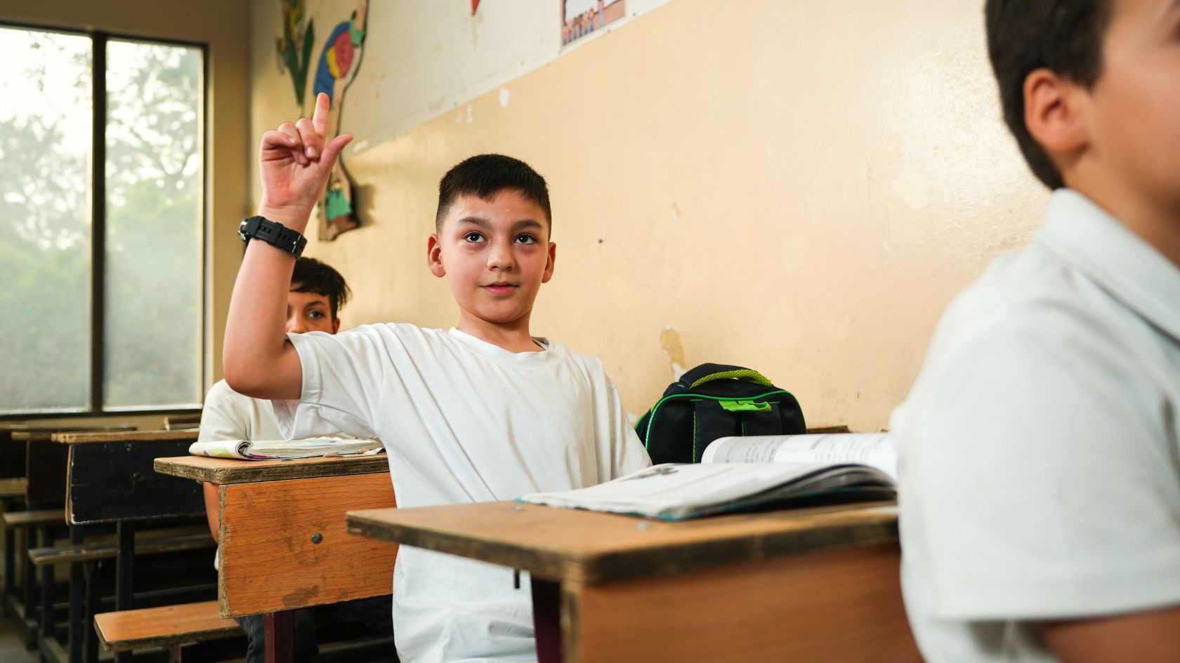 Junge hebt im Klassenzimmer die Hand, um eine Frage zu beantworten