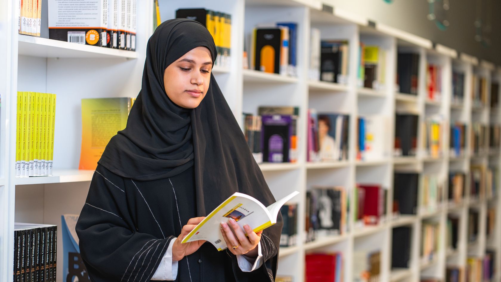 Junge Studentin liest ein Buch zwischen Bücherregalen in einer Bibliothek